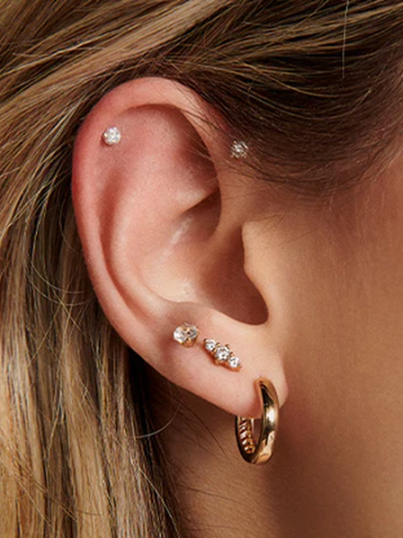 Close-up of an ear with gold hoop earrings and small stud earrings.