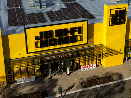 Aerial view of JB Hi-Fi retail store exterior with iconic yellow and black signage, solar panels on roof, and promotional banners at entrance