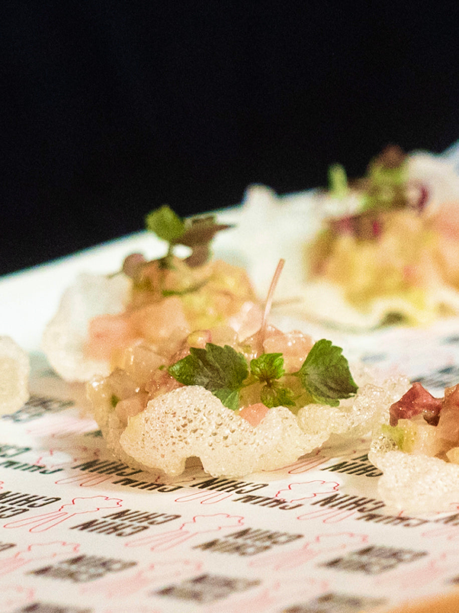 Close-up of gourmet appetizer featuring crispy prawn cracker topped with fresh garnish and microgreens on printed menu paper