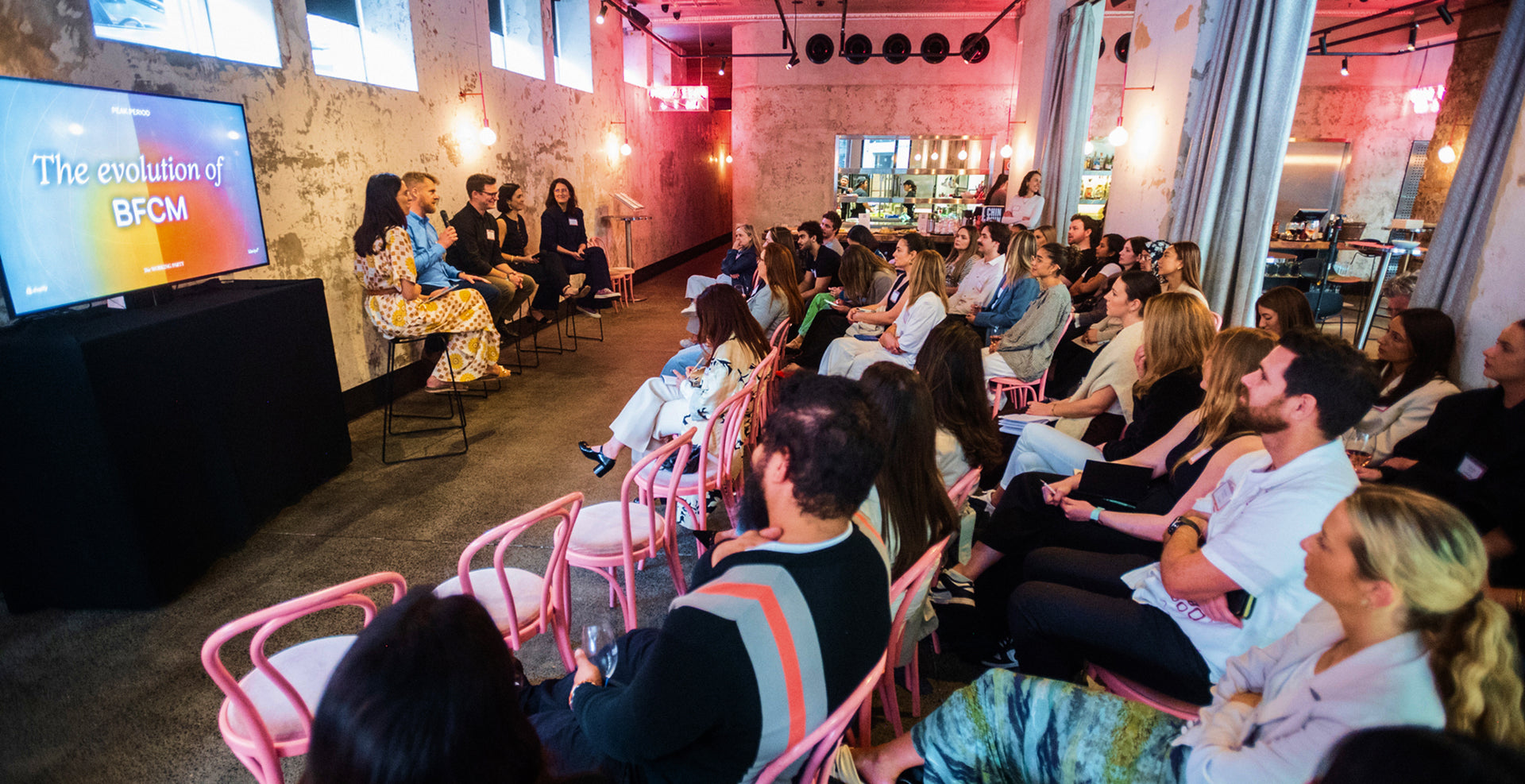 Audience attending a presentation in a modern indoor setting with a screen displaying 'The evolution of BFCM'.