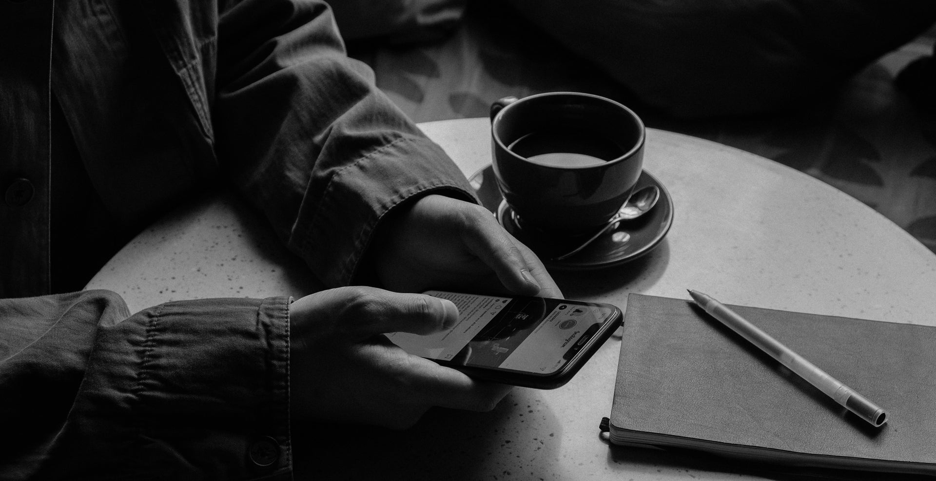 Person using a smartphone with a cup of coffee and notebook on a table.