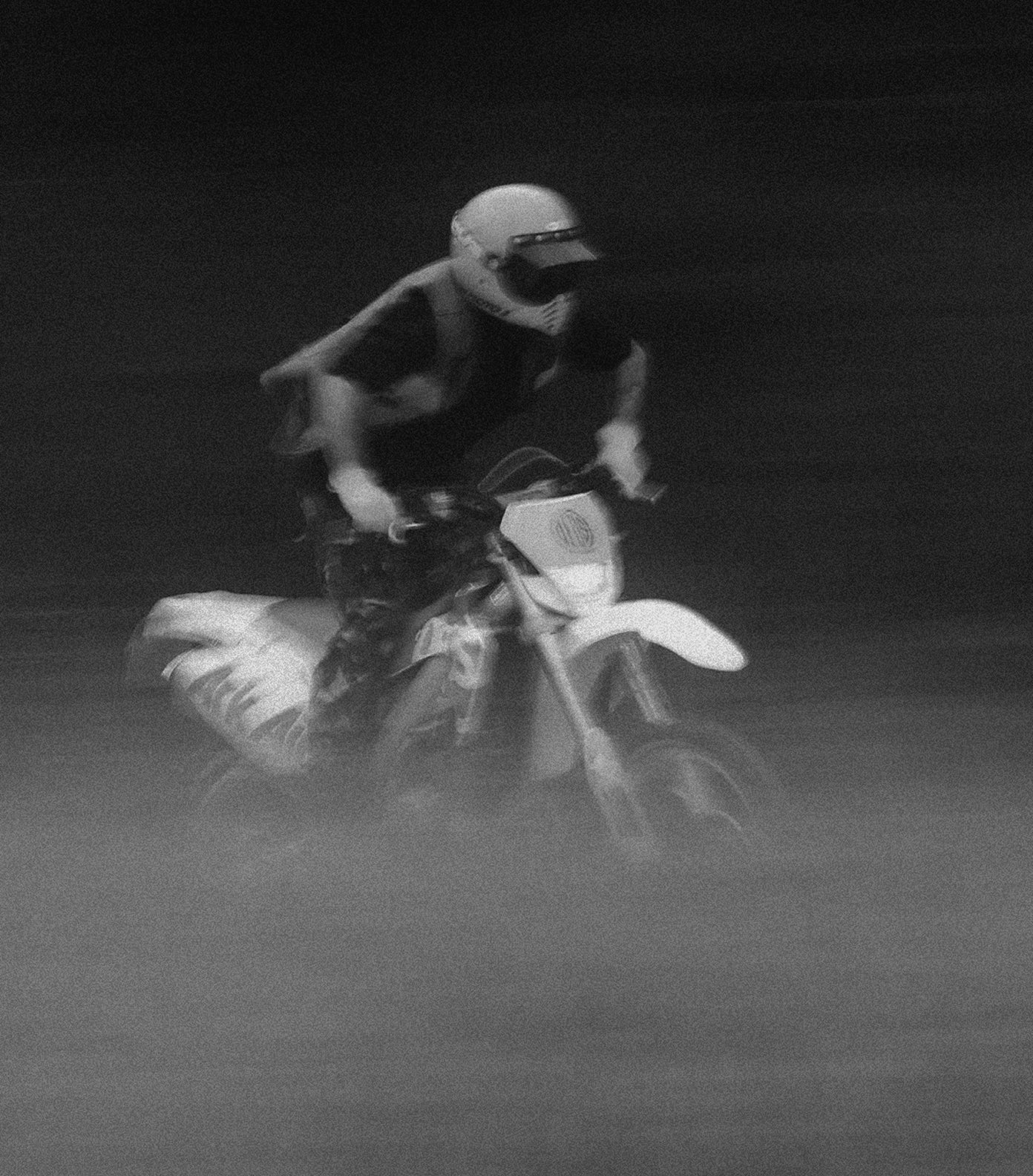 Person riding a dirt bike in a dark, foggy environment