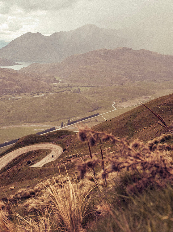 Scenic mountain landscape with winding roads through rugged terrain featuring lakes and misty peaks in muted vintage tones