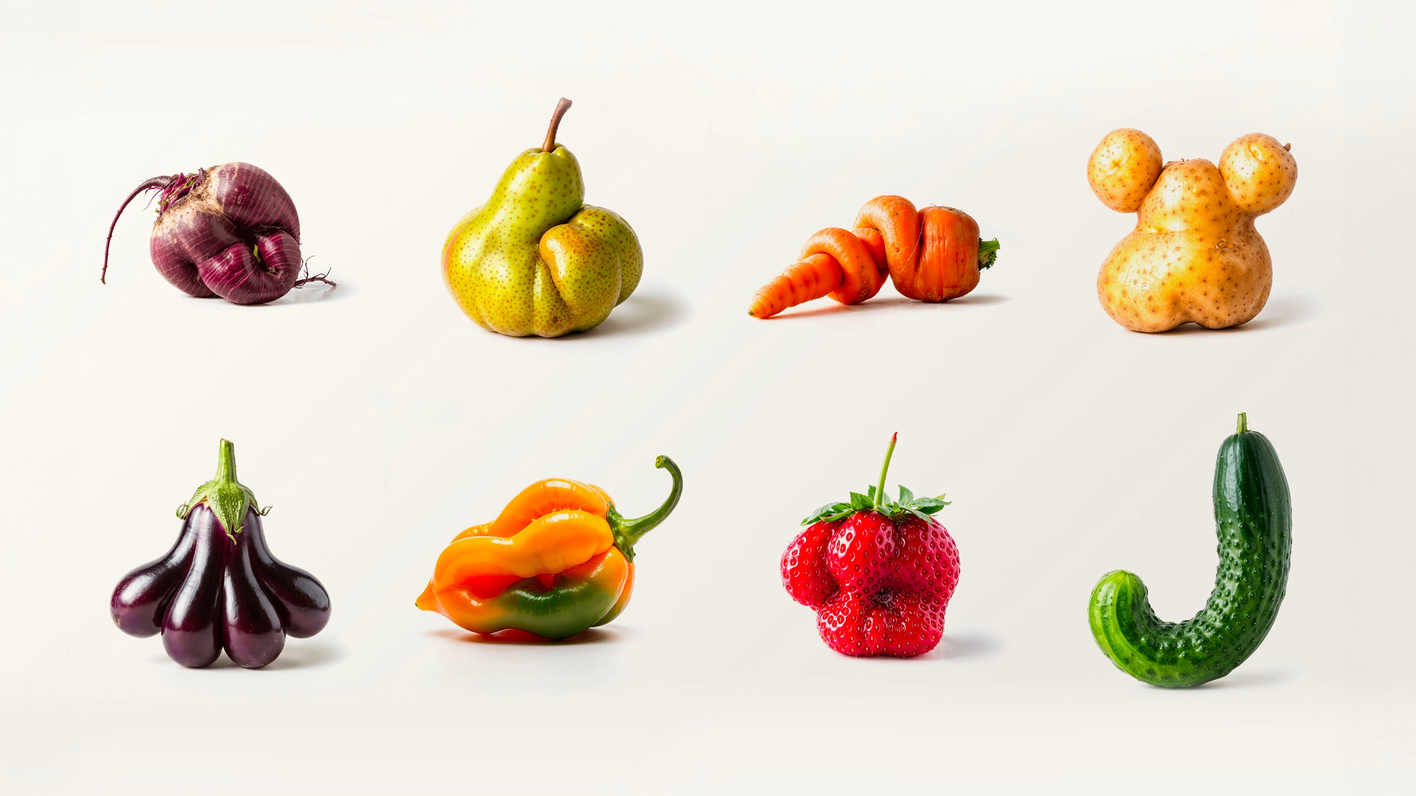 Oddly-shaped fruit and vegetables laid out on a plain background. 