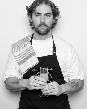 Man in a black apron holding a glass against a white background