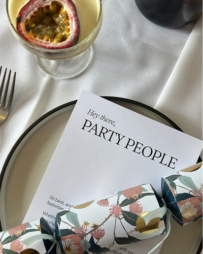 Elegant table setting with invitation card on white plate with passion fruit cocktail and Christmas cracker