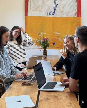 Team collaboration meeting around wooden table with laptops and fresh flower centerpiece in modern office with abstract artwork