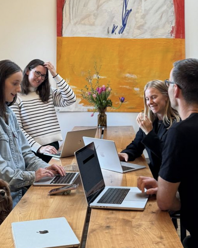 Team collaboration meeting around wooden table with laptops and fresh flower centerpiece in modern office with abstract artwork