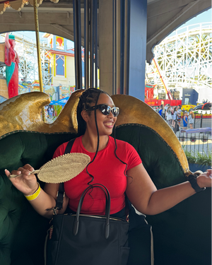 Person in red t-shirt and sunglasses sitting on decorative carousel horse at amusement park