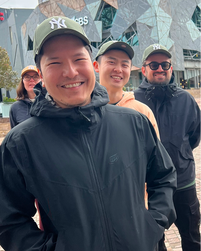 Group of colleagues wearing caps and black jackets smiling outside modern building on overcast day