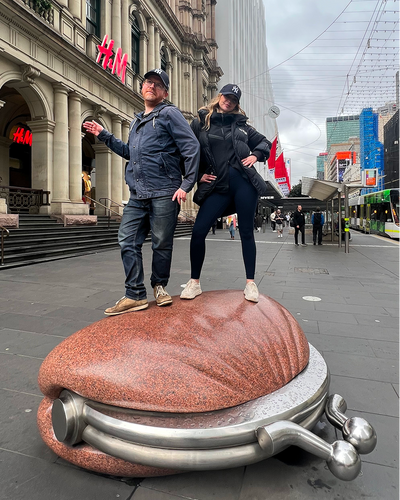 Two people posing on oversized sculpture in city plaza near historic architecture