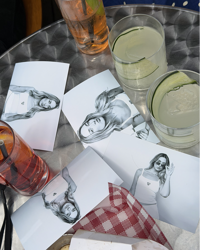 Overhead view of drinks table with black and white portrait photos on cocktail napkins surrounded by various beverages