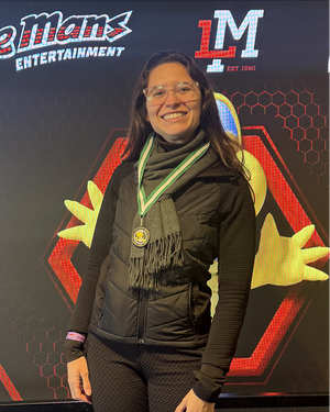 Woman wearing gold medal with yellow and black athletic outfit and scarf posing go-kart venue
