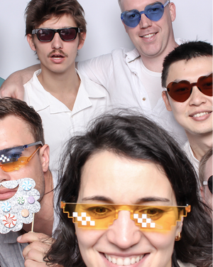 Group photo of five people wearing novelty sunglasses in photo booth