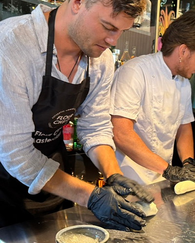 Chef in black apron kneading dough wearing black gloves in professional kitchen environment