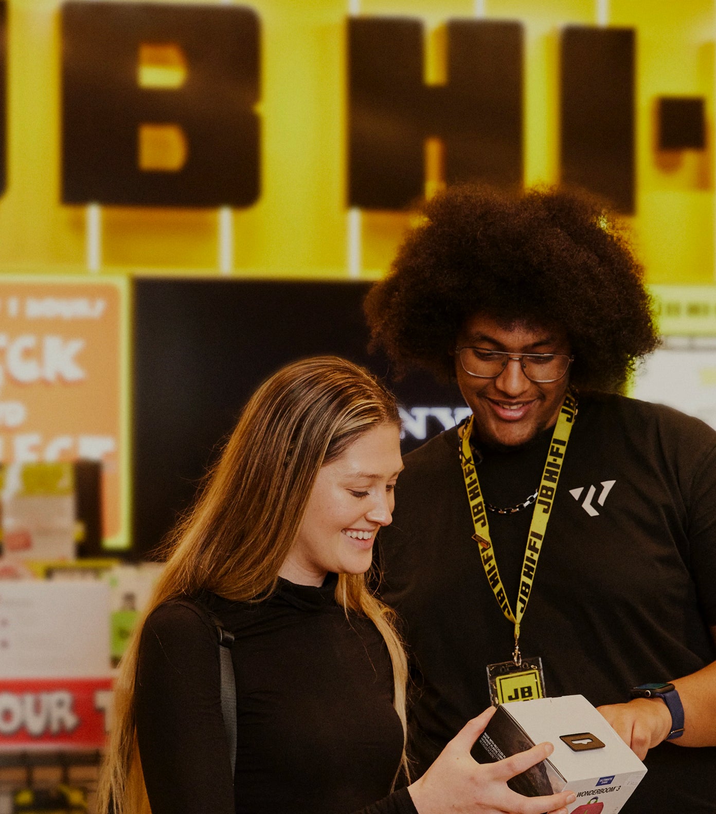 Two people looking at a product box with a colorful background in a JB Hi-Fi store