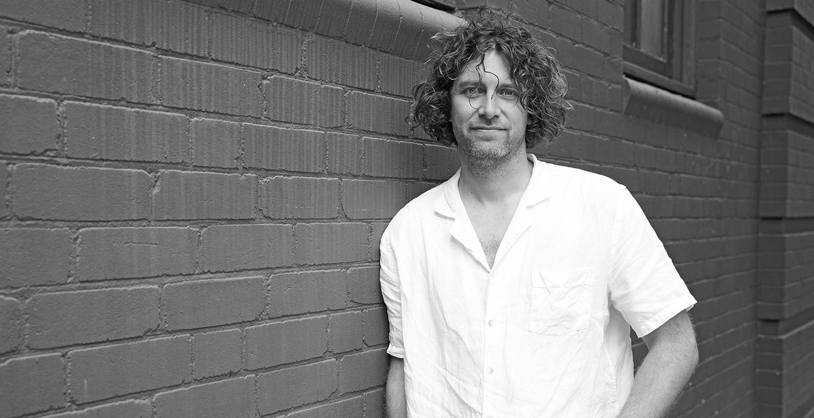 Man in a white shirt standing against a brick wall