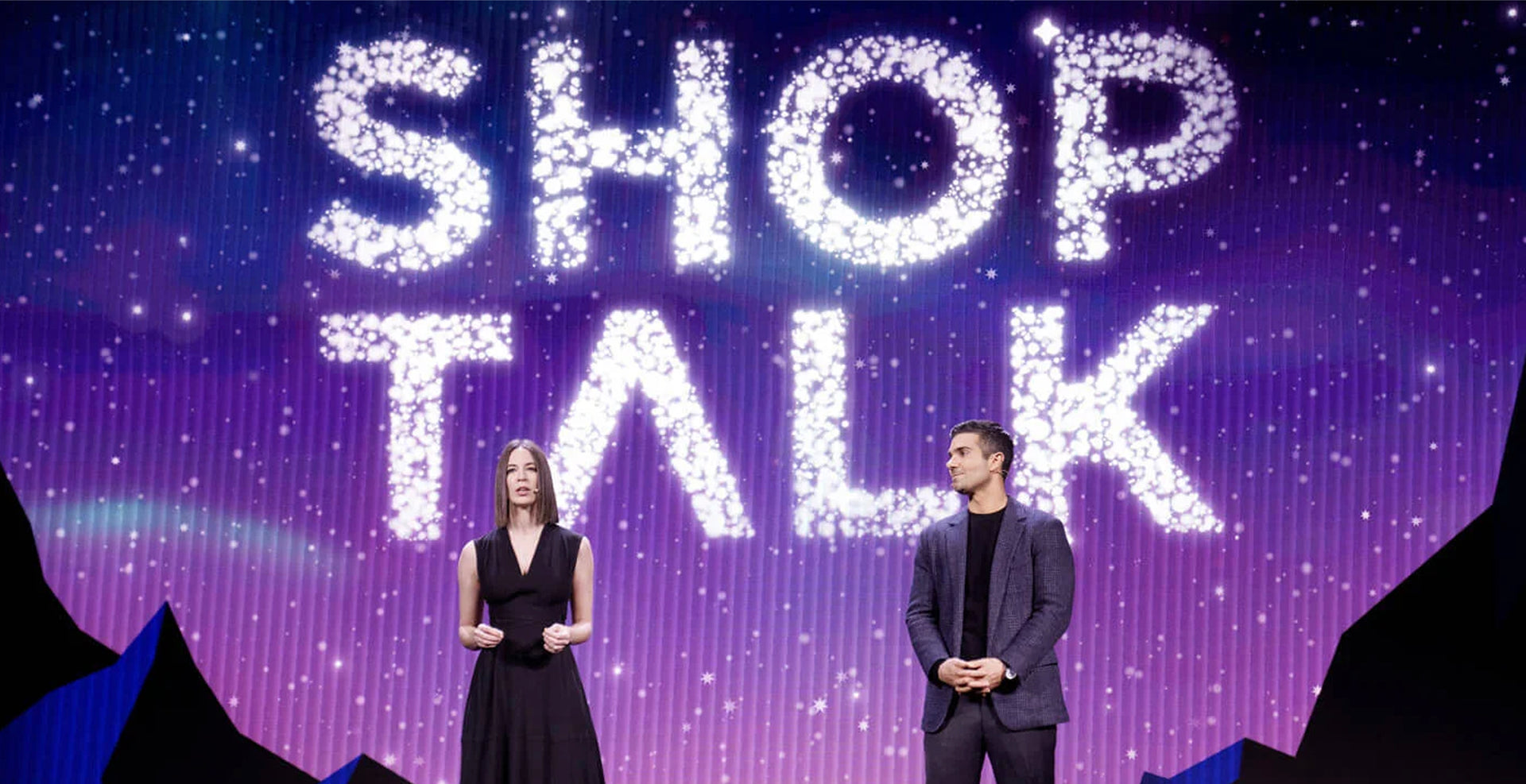 Two people standing on a stage with 'SHOP TALK' text in the background