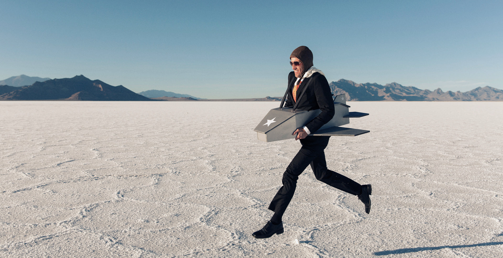 Person in a suit running across a desert landscape with mountains in the background