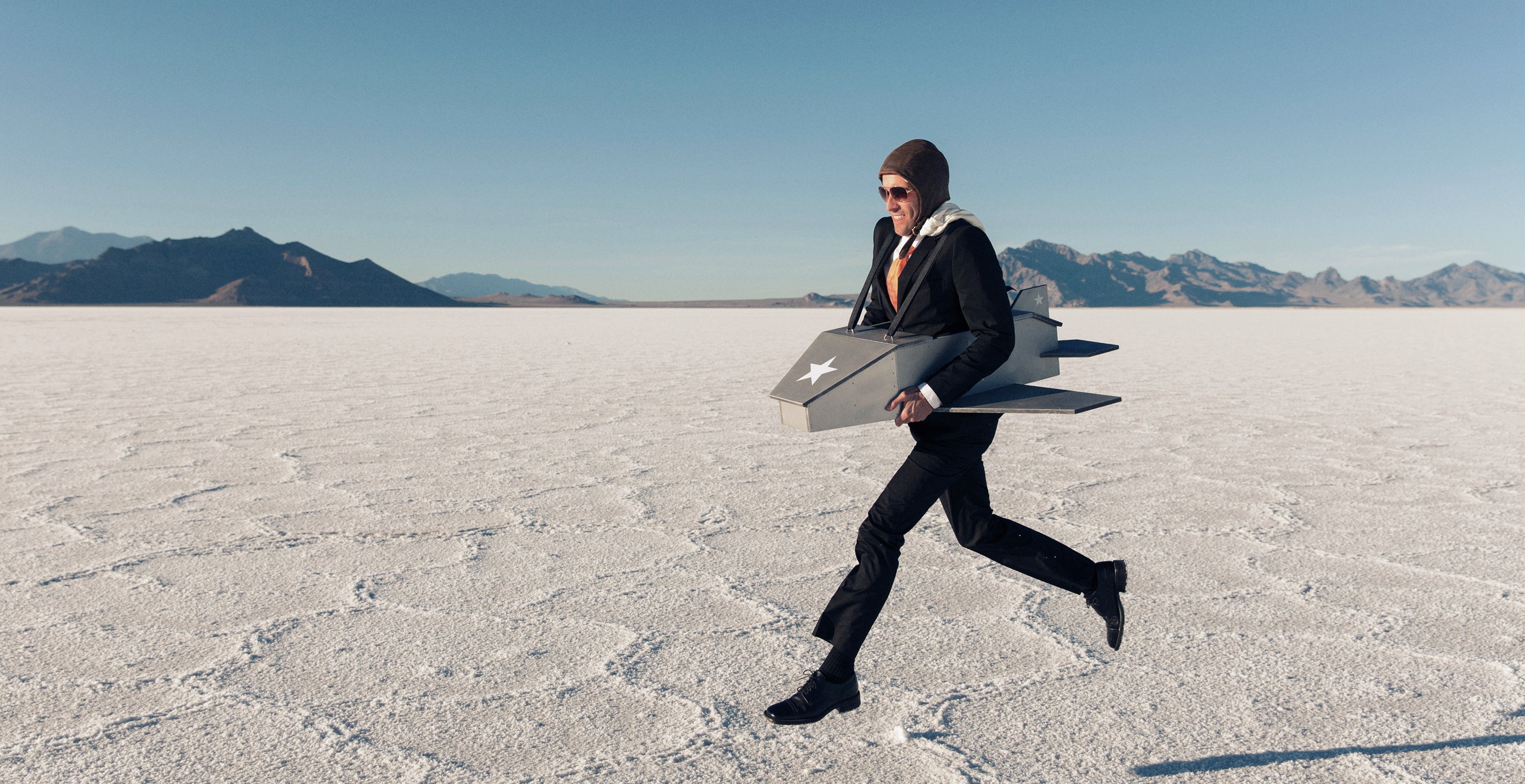 Person in a suit running across a desert landscape with mountains in the background