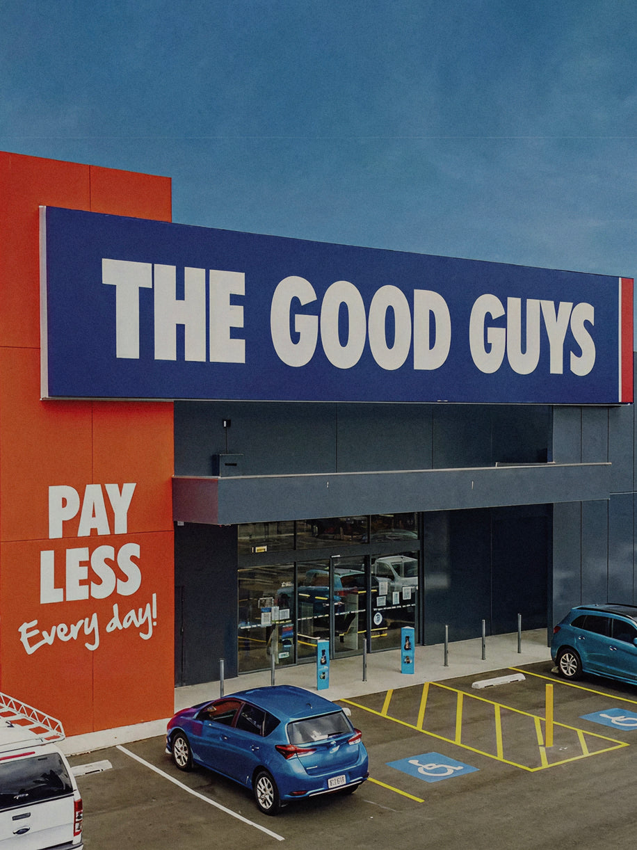 Exterior view of The Good Guys electronics retail store exterior with blue and white signage and red 'Pay Less Every Day' slogan